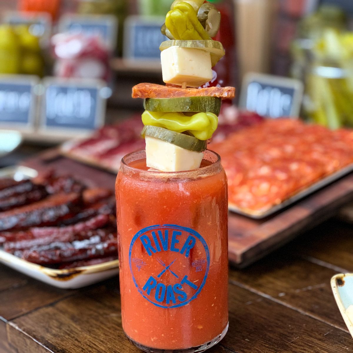 Bloody Mary with a large skewer of cheese chunks, olives, pickled peppers, and salami